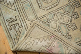 Folded vintage Melas rug with distressed beige geometric pattern, even wear, and hand-knotted foundation.