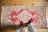 Distressed Oushak rug runner, dusty raspberry diamond medallion and beige field, with feet.