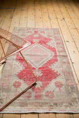 Distressed vintage Oushak rug with dusty raspberry diamond medallion, even wear showing foundation.