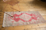 Distressed texture and secured corner of a vintage Oushak runner, revealing dusty raspberry and beige patterns.