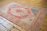 Distressed Oushak rug corner, featuring geometric border patterns in pale raspberry and teal.
