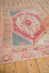 Distressed corner of vintage Oushak rug with pale raspberry, ivory, and ocean teal colors.