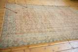 Oushak carpet end showing distressed pile, pale apricot vinery, and mint floral border.