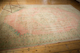 Distressed Oushak carpet corner showing faded pink, seafoam green floral motifs, and even wear.