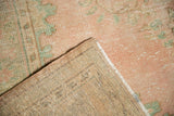 Folded corner of vintage Oushak rug shows distressed pink pile and hand-knotted foundation.