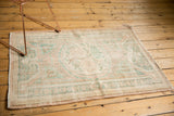 Distressed corner of a vintage Oushak rug showing pale blush, seafoam green, and visible foundation.