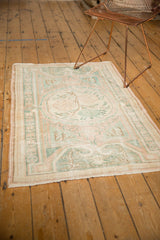 Distressed Oushak rug with faded pale blush, seafoam green, and ivory plant vinery.
