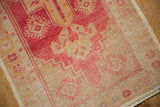 Corner of distressed Oushak rug, faded blush and ivory guls, low pile, fringed edge.