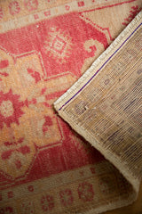 Distressed Oushak rug corner revealing faded red-ivory pile and hand-knotted reverse.