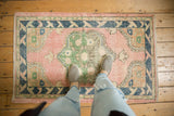 Feet on a distressed Oushak rug, highlighting soft pink, green floral medallion, navy border.