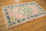 Distressed pink Oushak rug corner with navy leaf border and green floral medallion detail.