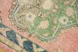 Distressed vintage Oushak rug with navy border, pink field, and green floral motifs.