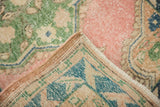 Distressed pink, green, blue Oushak rug corner revealing wear and secured edge.