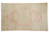 Distressed vintage Oushak carpet featuring a scalloped medallion and blush, seafoam vinery.