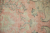 Distressed Oushak rug pile texture with faded blush, ivory, and pale seafoam vinery.