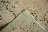 Vintage Oushak carpet's distressed beige pile, visible foundation, and intact side selvage.