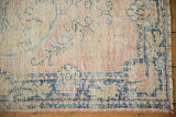 Distressed Oushak rug corner: worn indigo blue border, dusty blush field, and fringe.