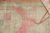 Faded pink, seafoam, and ivory tones on distressed Oushak rug with even wear.