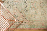 Close-up of distressed Oushak rug pile, showing faded green, blush, and brown tones.