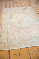 Distressed vintage Oushak rug end with scrolling blush and seafoam outlines, showing wear.