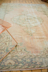 Distressed Oushak carpet's aged texture with soft pale rose and seafoam green patterns.