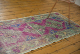 Distressed vintage Oushak runner's pale green floral border, purple field, and fringe.