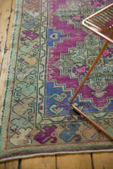 Close-up of distressed Oushak rug runner displaying worn purple field and faded floral border.