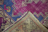 Distressed Oushak rug corner, showing vivid purple, denim blue pile, exposed foundation, and woven reverse.