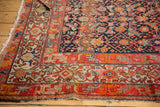 Antique Malayer rug corner, tattered fringe, tomato red geometric borders, navy Herati motif.