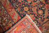 Antique Malayer rug corner showing navy Herati field, red geometric borders, and aged fringe.
