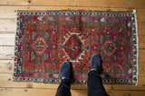 Vintage Karaja rug with a geometric triple medallion on brick red, shown with feet.