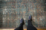 Person's feet on antique Mahal rug, showing worn Herati design with exposed foundation.