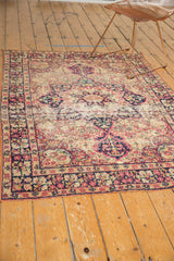 Secured side of the antique Kerman rug, showing navy and red floral border with light tatter.