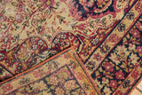 Folded antique Kerman rug showing fine floral border and threadbare red and navy patterns.