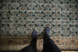 Distressed green and black field with pale apricot motifs, bordering a geometric vine design.
