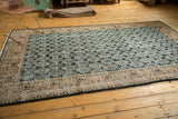 Distressed Oushak carpet corner, showing geometric apricot border and faded black floral motifs.