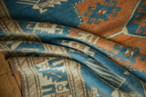 Folds of a distressed Oushak rug revealing sky blue, tangerine, and ivory geometric motifs.