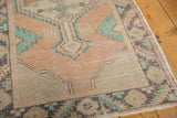Distressed Oushak rug's worn pile texture and lattice corner in apricot and mint green.