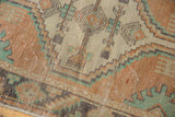 Texture and wear of a distressed Oushak rug runner, featuring dusty apricot and mint geometric outlines.
