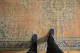 Decorative distressed texture on a vintage Oushak carpet with peach and blue floral patterns.