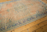 Distressed vintage Oushak carpet border with blue motifs and soft peach pile wear.