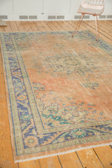 Distressed Oushak rug corner with faded pale rose field, dusty blue border, and worn fringe.