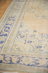 Vintage distressed Oushak carpet detail, showing pale sand field, dusty blue border, and worn floral patterns.