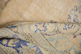 Distressed vintage Oushak rug showing worn pile, dusty blue patterns, and sand tones.