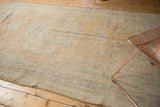 Decorative distressed Oushak carpet displaying textured pile, faded apricot sand, and subtle blue motifs.