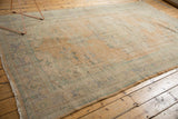 Fringed selvage and distressed pile texture of a vintage Oushak carpet with faded apricot and mint.