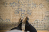 Feet on distressed vintage Oushak rug; rococo medallion in dusty blue, sand, and worn pile.
