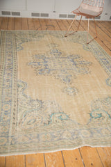Vintage distressed Oushak carpet with Rococo-style medallion, pale sand, and dusty blue tones.