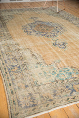 Distressed pile of vintage Oushak rug, with beige field and faded blue-green scalloped motifs.