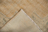 Folded vintage Oushak rug showing distressed beige pile, visible foundation, and side cord selvage.